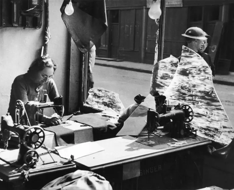Black and white photograph of a woman working amongst the broken glass of a tailor’s shop