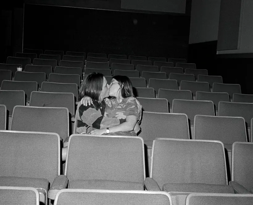 Black and white photograph of two people holding each other and kissing in a cinema