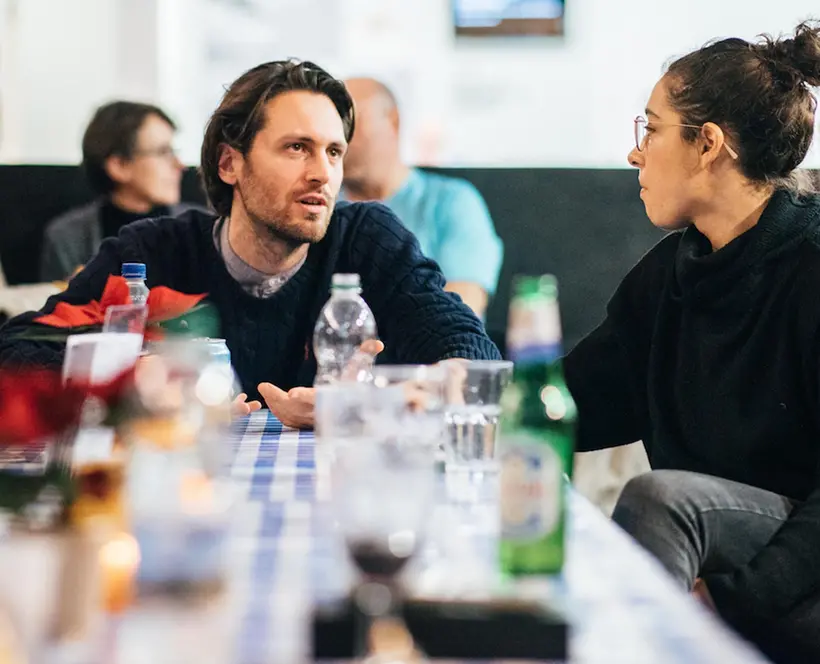 Two people are engaged in conversation in an informal but busy cafe environment